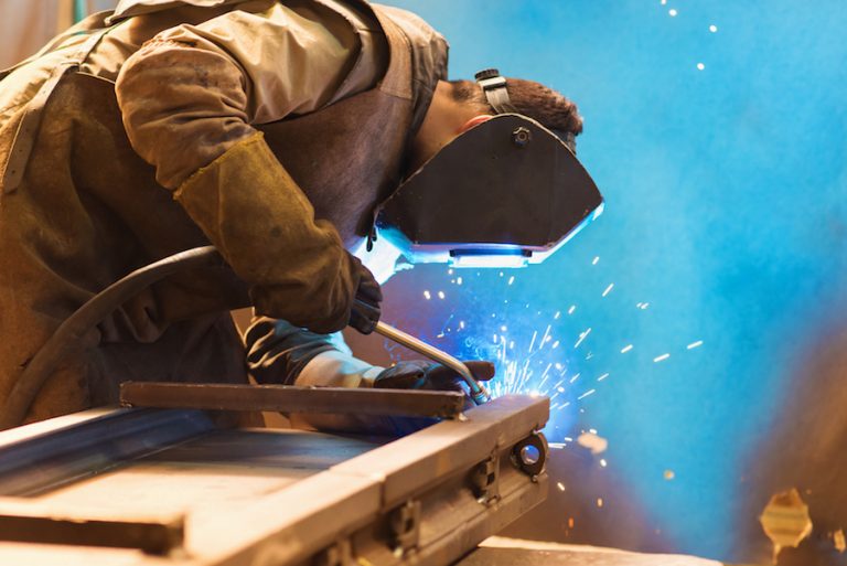 Young man with protective mask welding in a factory